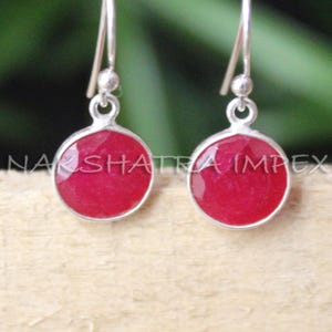 May include: A pair of silver dangle earrings with round, red gemstone drops.