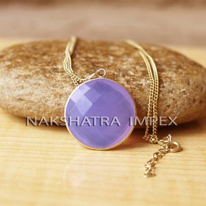 May include: A delicate gold chain necklace with a pendant featuring a large, round, faceted lavender chalcedony gemstone.