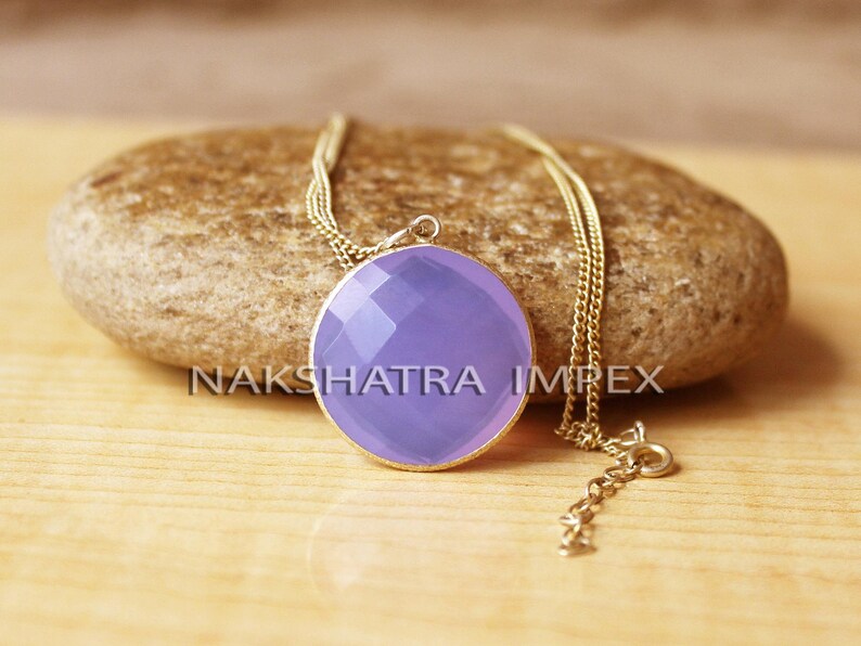 May include: A delicate gold chain necklace with a pendant featuring a large, round, faceted lavender chalcedony gemstone.