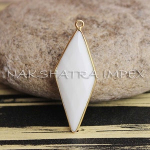 Peut inclure: Un pendentif en pierre blanche avec un sertissage doré. Le pendentif est en forme de diamant et a une finition lisse et polie.
