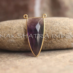 Op de afbeelding: Een vergulde hanger met een paarse amethist edelsteen in een traanvorm. De hanger heeft twee springringen om aan een ketting of koord te bevestigen.