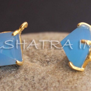 May include: A pair of gold earrings with light blue square-shaped gemstones. The earrings have a post back closure.