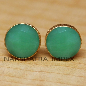 May include: A pair of gold earrings with green gemstone accents. The earrings have a round shape and a textured gold setting.