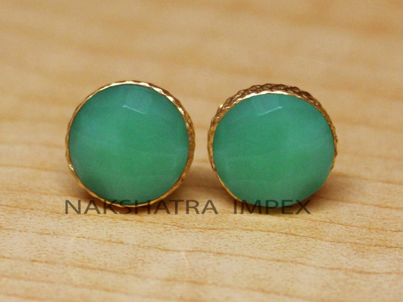May include: A pair of gold earrings with green gemstone accents. The earrings have a round shape and a textured gold setting.