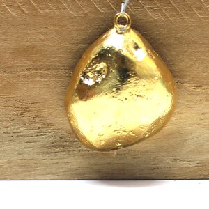 May include: A gold-colored pendant shaped like a teardrop with a textured surface.
