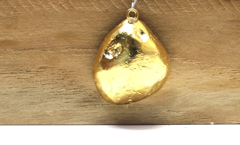 May include: A gold-colored pendant shaped like a teardrop with a textured surface.