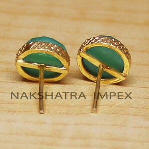 May include: A pair of gold earrings with green gemstone cabochons. The earrings have a simple design with a gold post and a round cabochon.