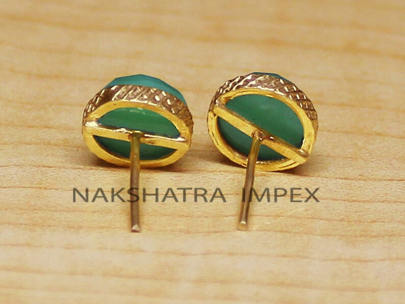 May include: A pair of gold earrings with green gemstone cabochons. The earrings have a simple design with a gold post and a round cabochon.