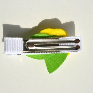 May include: A green and yellow felt flower hair clip with a white ribbon and a silver alligator clip.