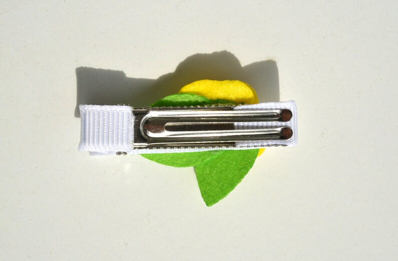 May include: A green and yellow felt flower hair clip with a white ribbon and a silver alligator clip.