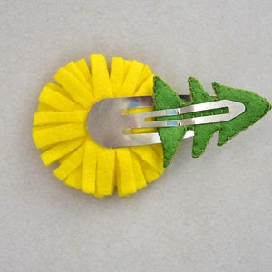 May include: A yellow felt flower with a green felt leaf attached to a silver hair clip.