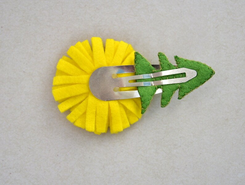 May include: A yellow felt flower with a green felt leaf attached to a silver hair clip.