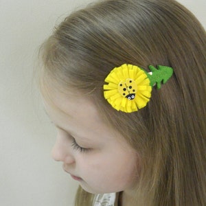 May include: A yellow felt flower hair clip with a ladybug in the center. The flower has a green felt leaf attached to the side.