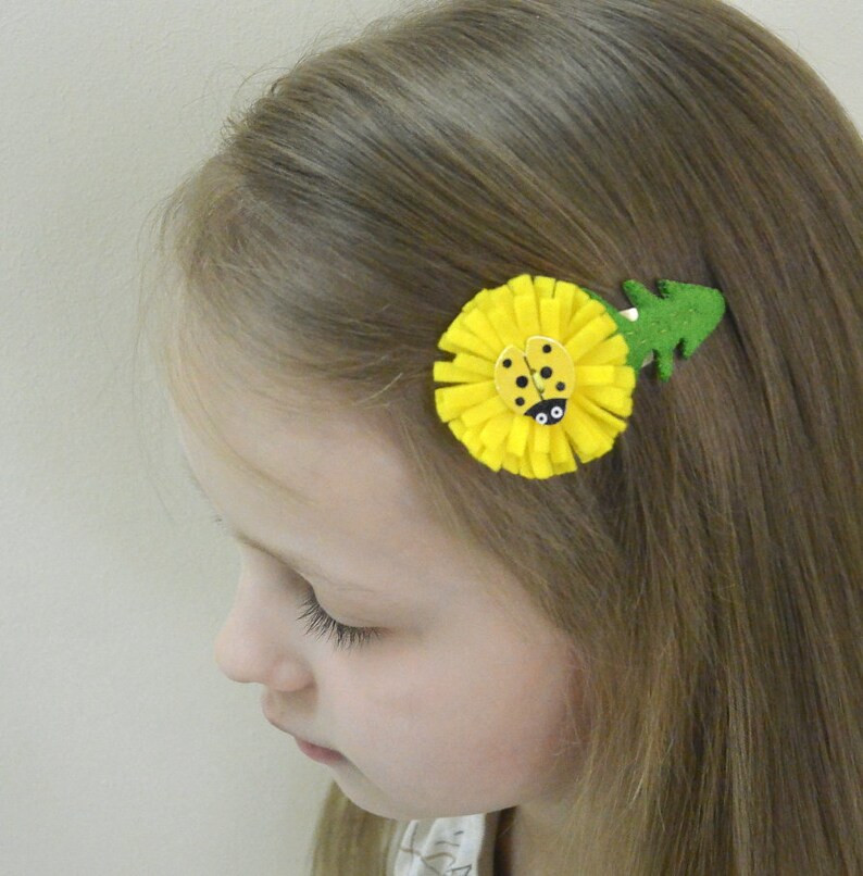 May include: A yellow felt flower hair clip with a ladybug in the center. The flower has a green felt leaf attached to the side.