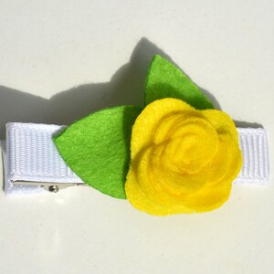 May include: A yellow felt flower with green felt leaves attached to a white ribbon with a metal clip.