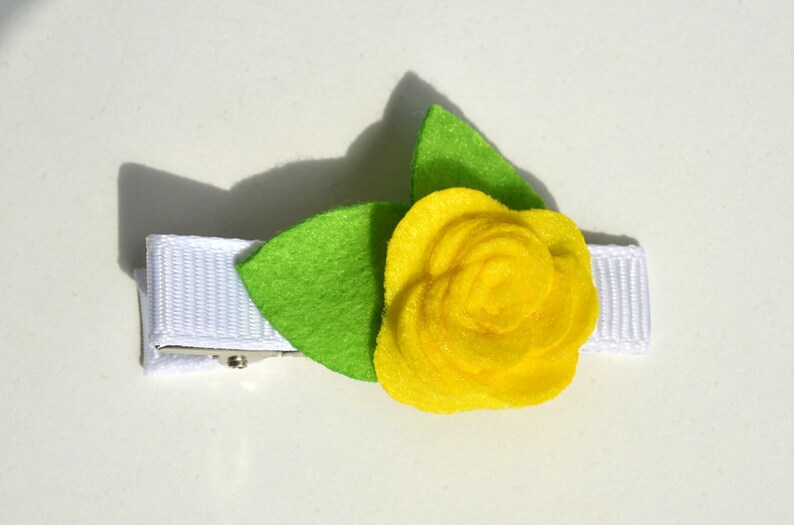 May include: A yellow felt flower with green felt leaves attached to a white ribbon with a metal clip.
