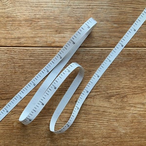 May include: White measuring tape with black markings on a wooden surface. The tape is in a loop and is about 76 cm long.