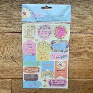 May include: A sheet of 34 die-cut stickers with various sweet treat designs and messages. The stickers feature a variety of colours, including pink, blue, yellow, and brown. The messages on the stickers include "Hey there Sweetie!" "With Love" "A little treat for you!" "Sprinkled with Love!" "With all my Love" "Especially for You" "Thinking of you" "Birthday wishes" "Made with Love" "Hello!" "You're a little Gem!" and "Thank You".