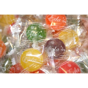 May include: Close-up of a pile of individually wrapped candies in various colors. The candies are round and have the text "Eda's" printed on the wrappers. Colors include yellow, green, red, and brown.