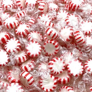 May include: A close-up of a large pile of individually wrapped red and white peppermint candies.