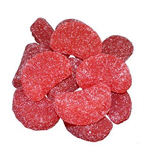 May include: A close-up of a pile of red, candy-coated gummy fruit slices. The gummies are shaped like half-circles and have a grainy texture.