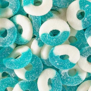 May include: A close-up shot of a pile of blue and white gummy rings. The rings are coated in sugar crystals, with a half-and-half color scheme. The blue sections are a vibrant turquoise, while the other half is white.
