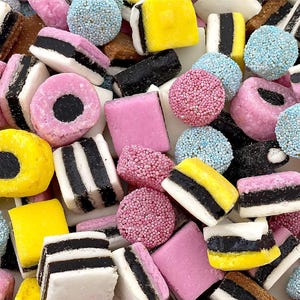 May include: A variety of colorful candy, including black and white licorice, pink and yellow squares, and round candies with sprinkles.