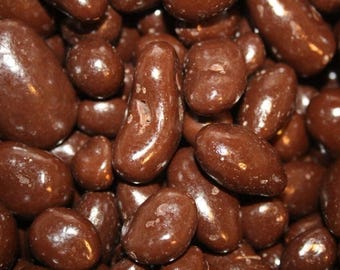 May include: A close-up of a large pile of chocolate-covered almonds. The almonds are all the same size and shape, and they are covered in a smooth, dark chocolate.