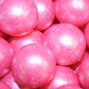 May include: A close-up of pink gumballs with a pearlescent finish. The gumballs are piled high and create a colorful and festive background.