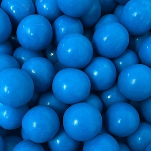 May include: A close-up shot of a pile of bright blue gumballs. The gumballs are round and have a smooth, glossy surface. The image is tightly framed, filling the entire view with the candy.