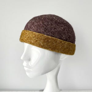 May include: A brown and gold knitted beanie with a wide band. The beanie is made of a soft, textured yarn.