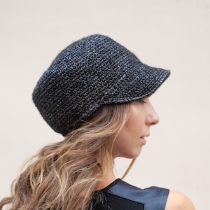 May include: A grey crocheted hat with a brim. The hat is being worn by a person with long, wavy hair.