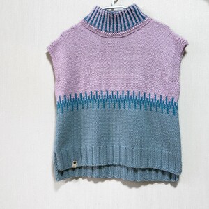 May include: A sleeveless knitted sweater with a high neck. The sweater is a gradient of pink and blue colors with a blue and white patterned band.