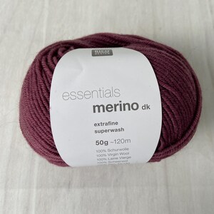 May include: A ball of burgundy-colored merino wool yarn with a white label. The label reads "essentials merino dk extrafine superwash" and lists the weight as 50g ~120m. The yarn is 100% virgin wool.
