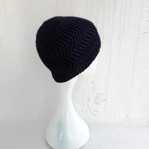 May include: A black knit beanie with a chevron pattern. The hat is displayed on a white mannequin head against a white background. The beanie's textured design is visible, showcasing the zig-zag pattern.