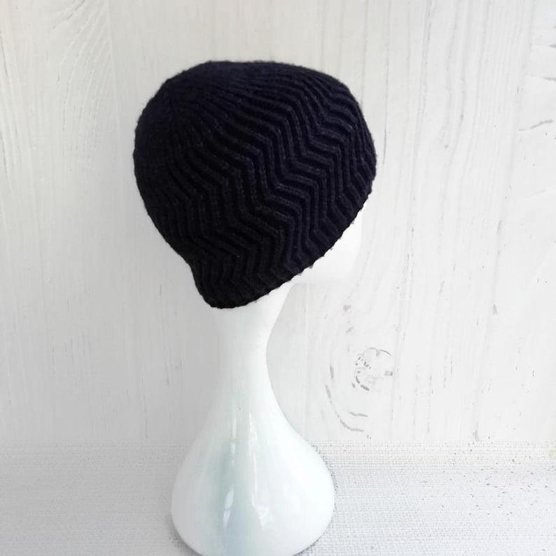May include: A black knit beanie with a chevron pattern. The hat is displayed on a white mannequin head against a white background. The beanie's textured design is visible, showcasing the zig-zag pattern.