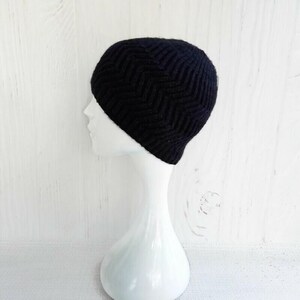 May include: A dark navy blue knit beanie with a chevron pattern. The hat is displayed on a white mannequin head against a white background. The beanie is made of a soft, textured material, perfect for cold weather.