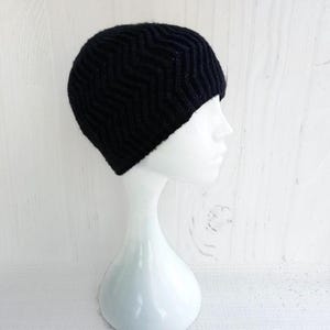May include: A black knit beanie with a chevron pattern. The hat is displayed on a white mannequin head. The beanie is made of a soft, textured material, perfect for cold weather. The hat is a stylish accessory.