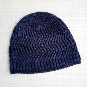May include: A navy blue knit beanie with a chevron pattern. The hat is made of a textured yarn and has a ribbed brim. The beanie is a winter accessory.