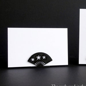 May include: Three white business cards are displayed on decorative fan-shaped card holders. The holders are black, gold, and gray. The cards are 3.25 inches by just over 2 inches.