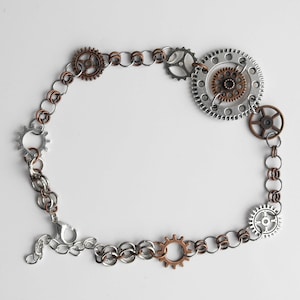 May include: A silver and copper chain bracelet with multiple gear charms. The bracelet has a lobster clasp closure.