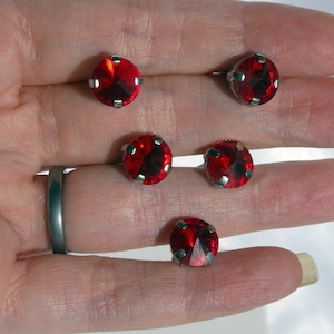 May include: Five red round rhinestones with silver settings. The rhinestones are on a hand.