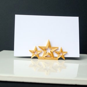 May include: A gold-colored, three-dimensional star-shaped card holder with a blank white card.