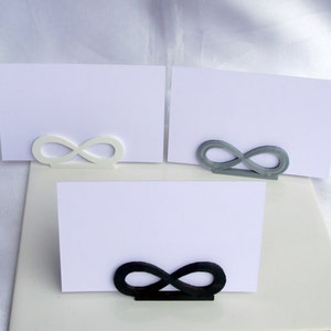 May include: Three white card holders with infinity symbol designs. The holders are in white, gray, and black.