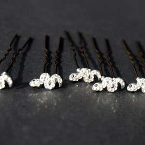May include: Set of eight silver hair pins with a rhinestone snake design. Each pin has a black eye detail.