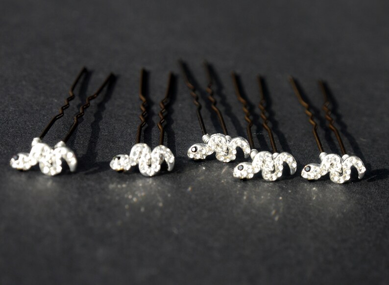 May include: Set of eight silver hair pins with a rhinestone snake design. Each pin has a black eye detail.
