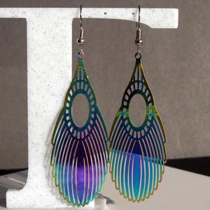May include: A pair of iridescent earrings with a teardrop shape and a cut-out design. The earrings are made of metal and have a silver hook.