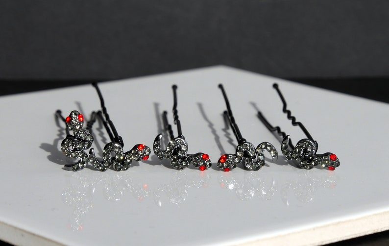 May include: Set of six black hair clips with a rhinestone snake design. Each snake has red eyes.
