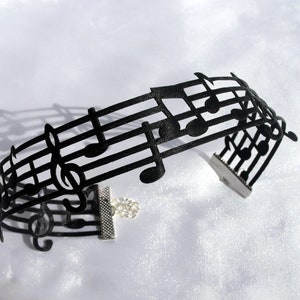 May include: Black choker necklace featuring a musical note design. The necklace is made from a flexible material and has a clasp fastening.