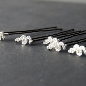 May include: Set of six black hair pins with silver rhinestone accents in the shape of a wavy line.